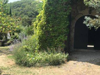 Toegangspoort met oude stenen muur en open houten deuren omgeven door groen en lavendel in rustige tuin bij le mas d'aunas