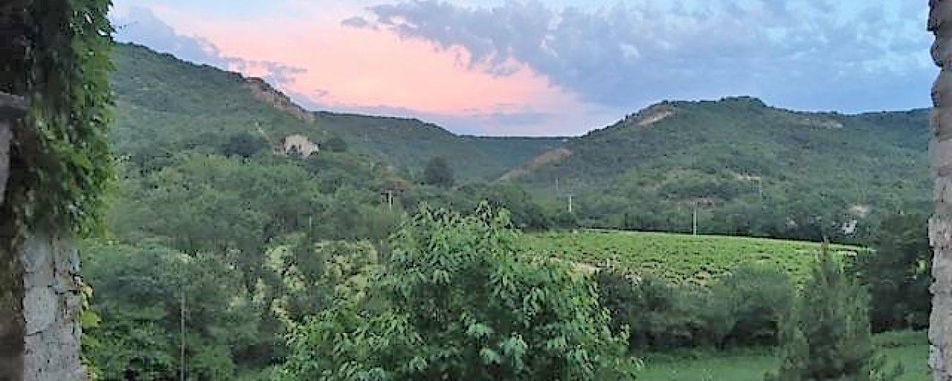 Uizicht vanuit ruwe stenen raam op groene heuvels en tuin in zuid-ardèche rustige natuurlijke omgeving